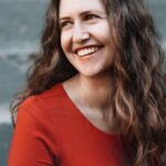 woman looks off-camera to the left smiling in an orange long-sleeved shirt